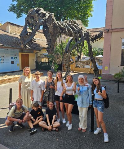 Lehrerin steht mit Schüler/innen vor einem Dinosauriermodell
